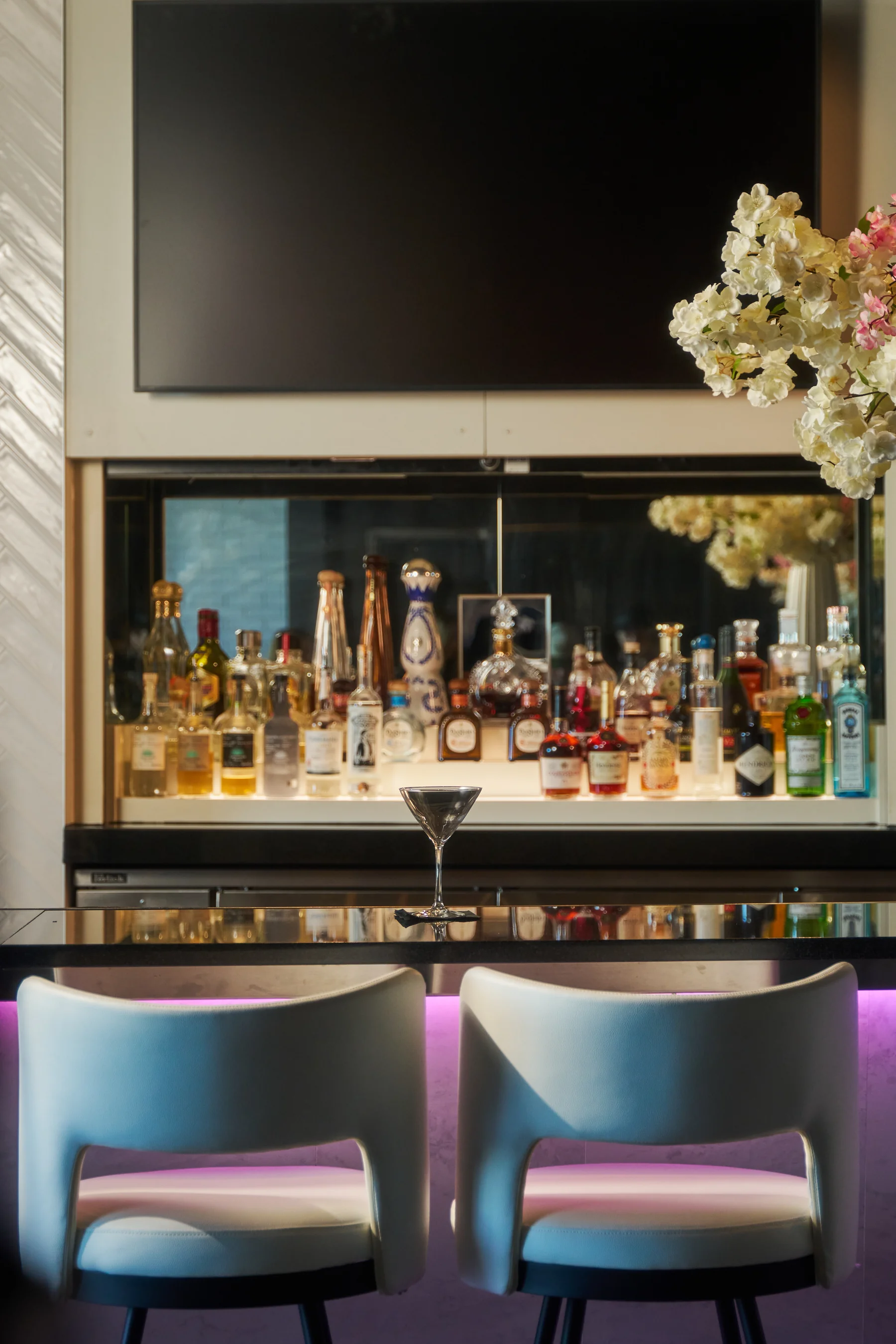 The STK Niagara Falls back-bar with the illuminated bottle library, a lone martini on the counter, and cherry blossoms in the corner