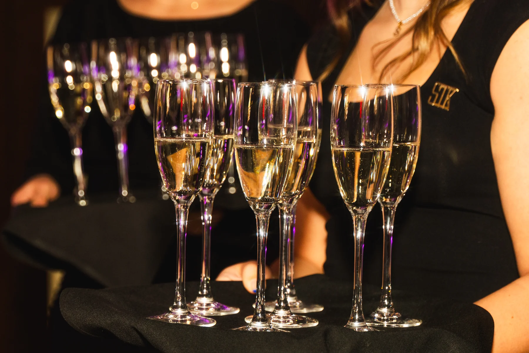 A tray of champagne flutes carried through the STK Niagara Falls dining room by a server in STK black