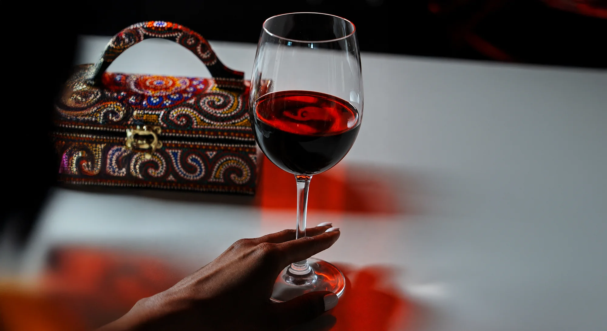 A hand holding a glass of red wine beside a beaded jewel-box at STK Niagara Falls