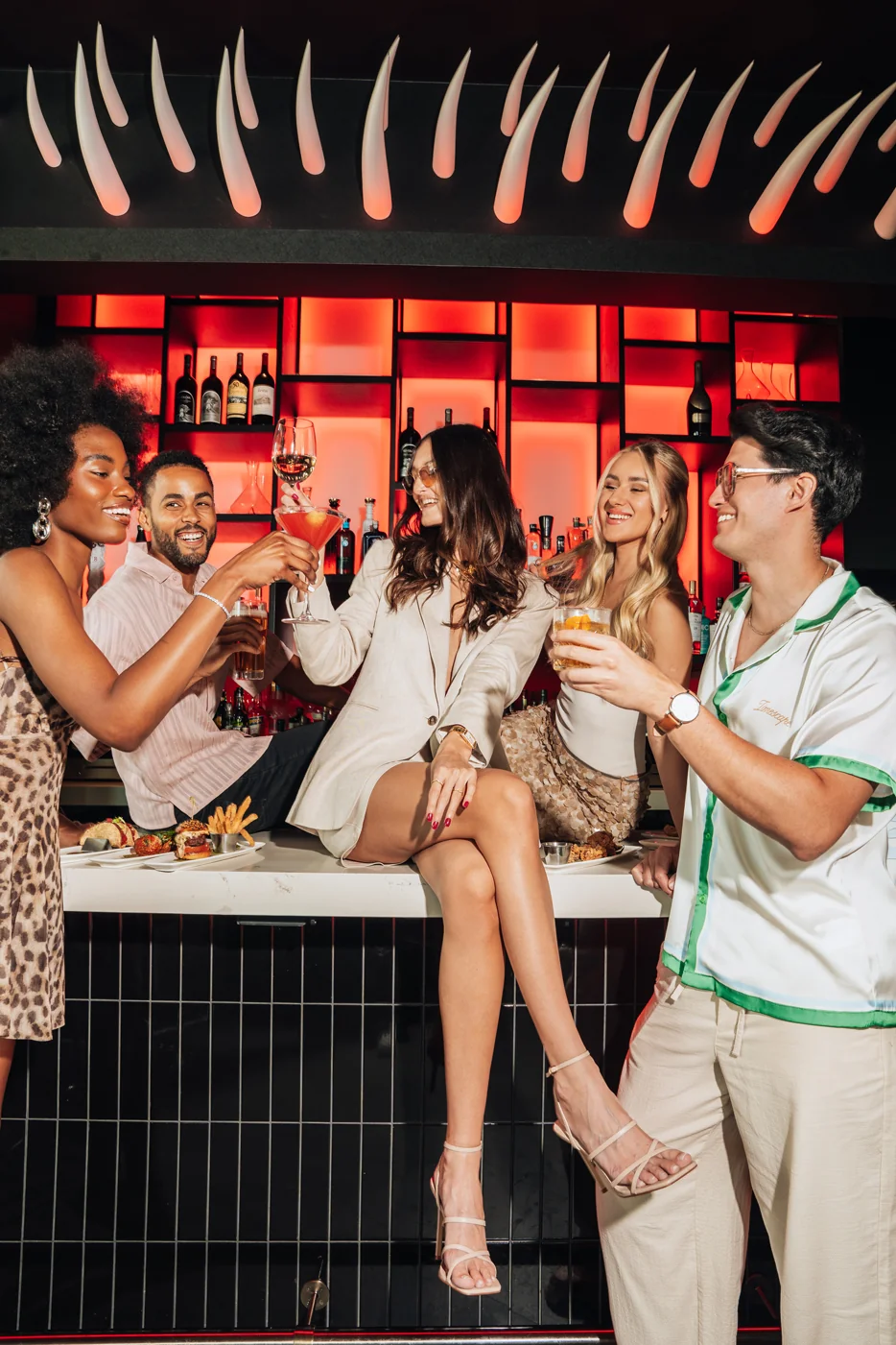 Five friends laughing and toasting cocktails at the STK Niagara Falls bar under the signature red-lit back-bar