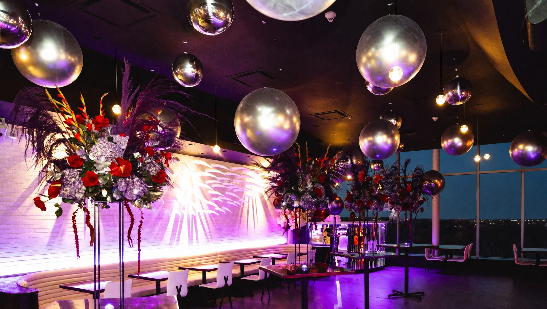 A full buyout setup at STK Niagara Falls with mirrored sphere installations, towering red and feather florals, purple uplighting, and the city view through the panoramic windows