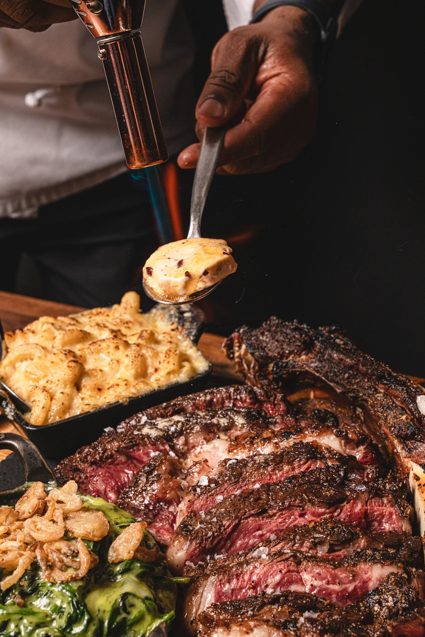 Tomahawk steak being torch-finished with bone marrow butter alongside truffle mac and creamed spinach at STK Niagara Falls