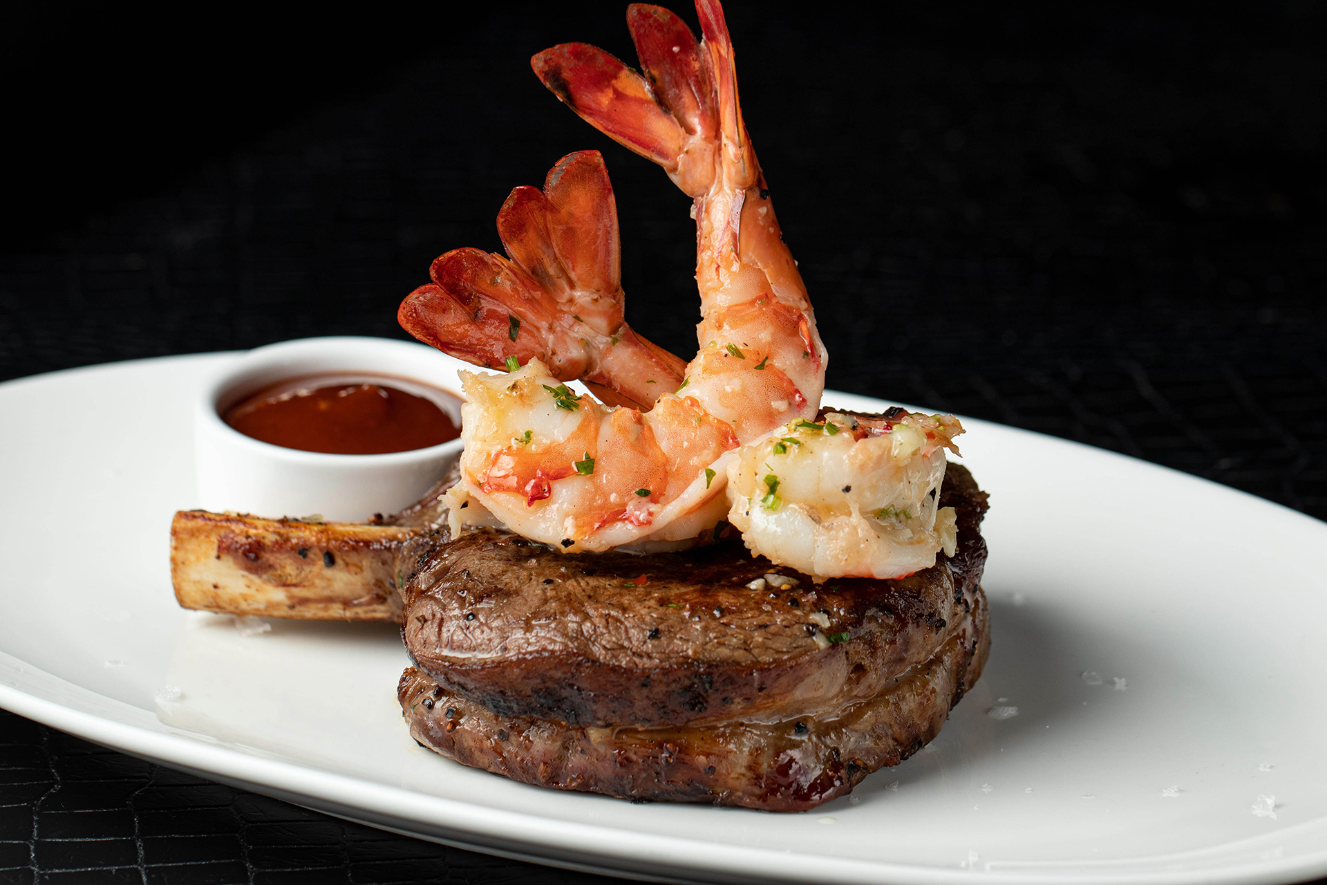 A bone-in filet crowned with garlic-butter cocktail shrimp, served with cocktail sauce on a crisp white plate at STK Niagara Falls