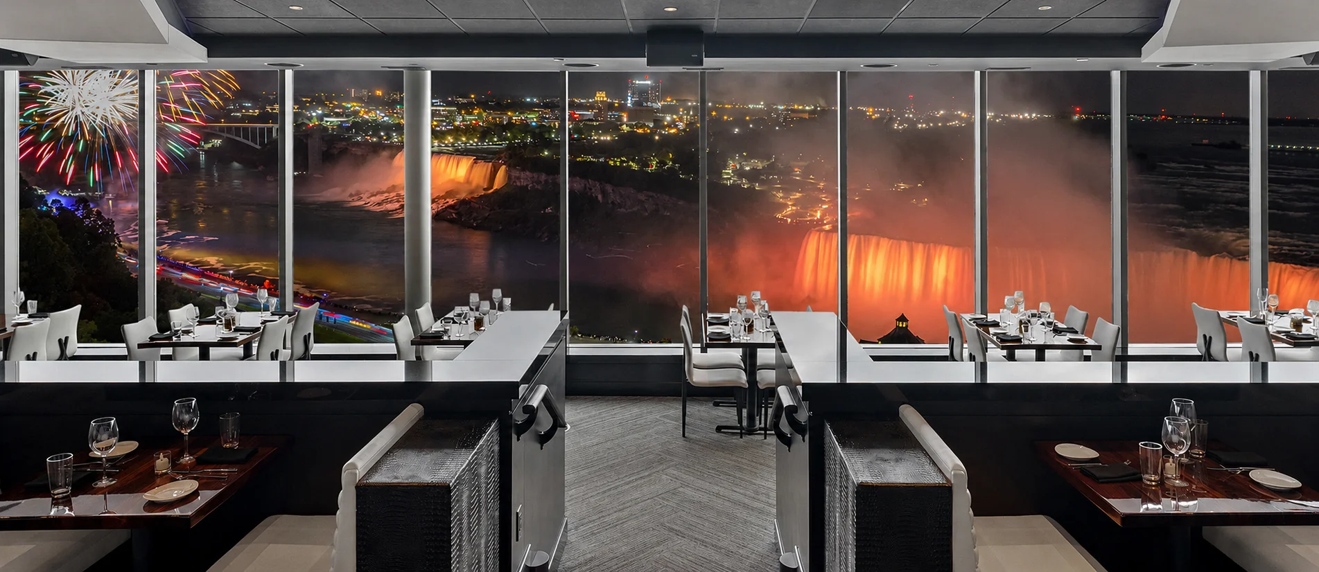 STK Niagara Falls — panoramic dining room with the illuminated Falls and fireworks visible through floor-to-ceiling windows